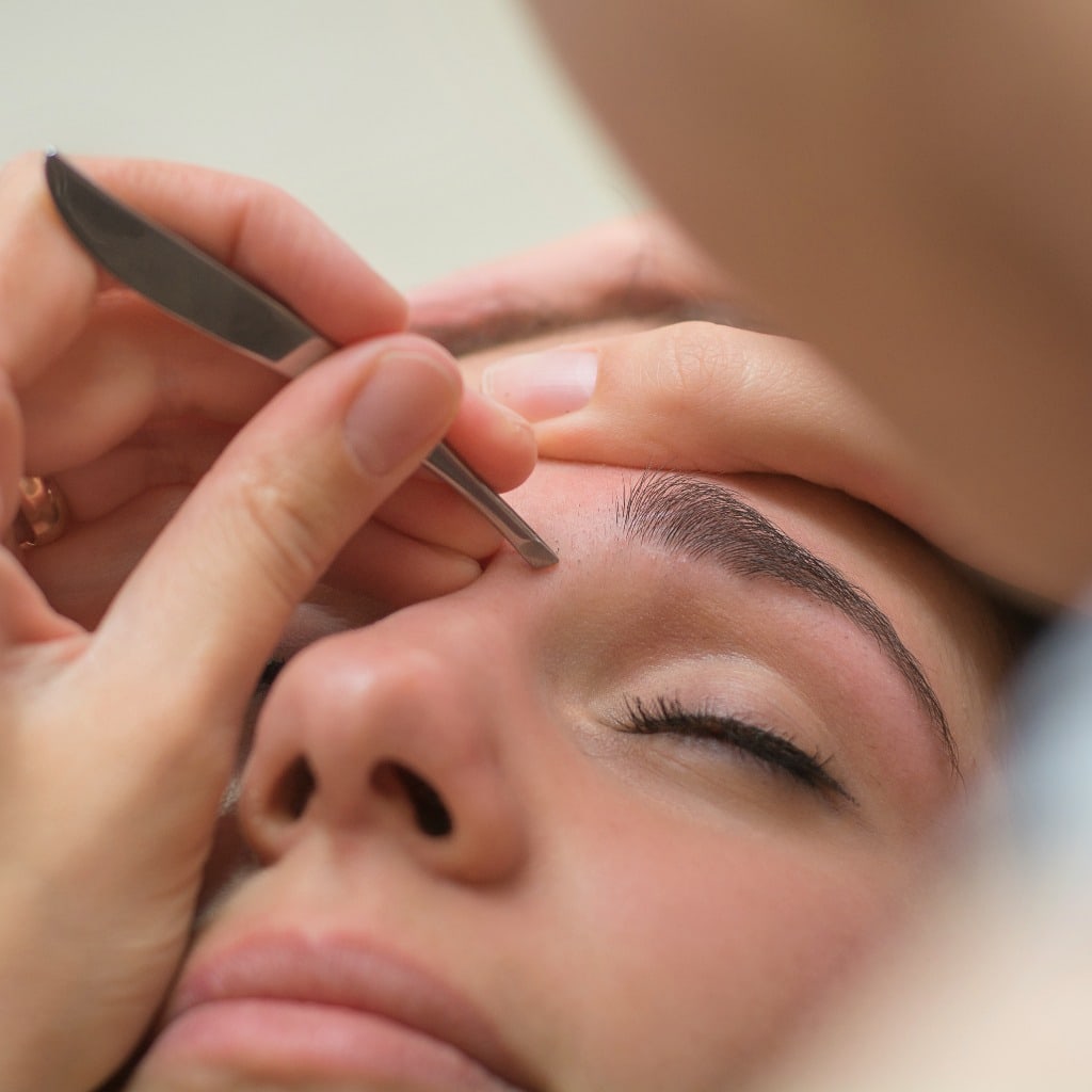 Beautiful young woman gets eyebrow correction procedure. Young woman painting her eyebrows in beauty saloon. close-up of a young woman plucking eyebrows with tweezers