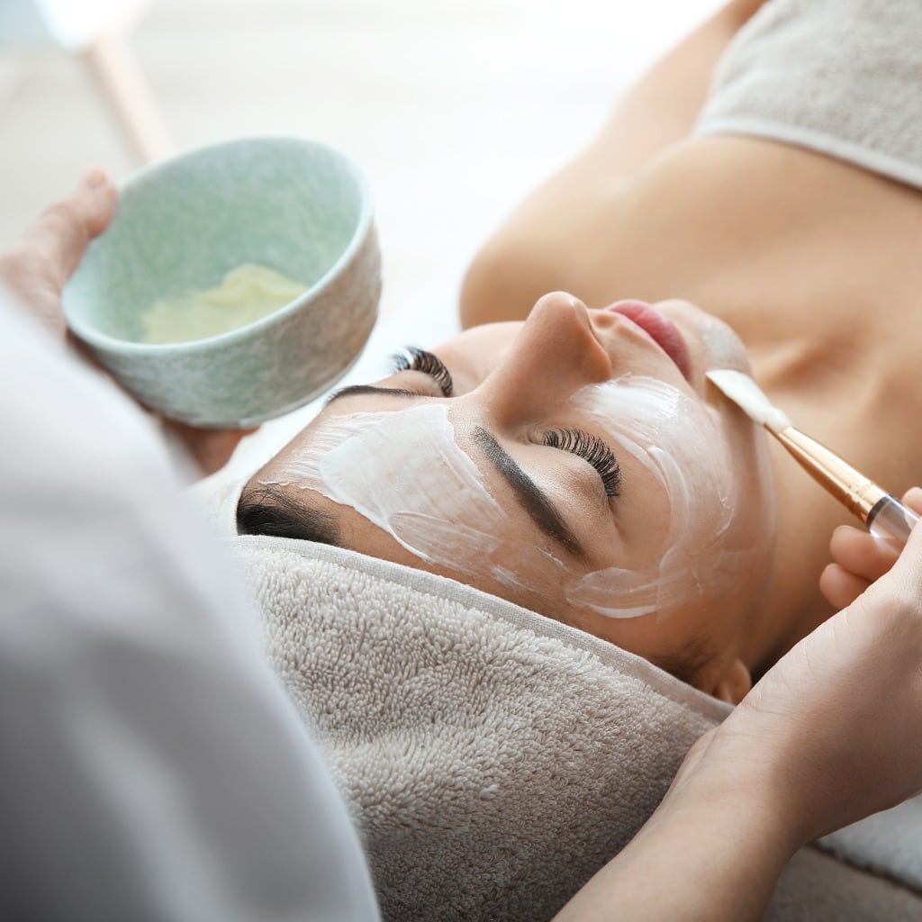 Cosmetologist applying mask on client's face in spa salon